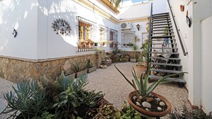Un patio con escaleras, plantas en macetas y un edificio blanco con suelo de baldosas.