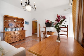 A wooden dining table with a vase of flowers, a wooden cabinet with books, and a white sofa in a well-lit room with a chandelier. - Apartment 'Caracola' with Private Terrace, Wi-Fi and Air Conditioning (Chipiona)