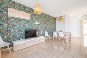 Un saló modern amb paper tapissat amb motius, una televisió de pantalla plana, zona de menjador amb cadires i taula de dinar de fusta.