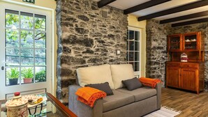 Eine Steinsäule, ein graues Sofa mit Kissen, eine Holzkommode und ein Fenster mit Pflanzen.