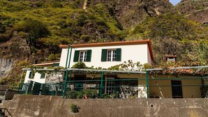 Ein weißes Gebäude mit grünen Fensterläden, einer Steinmauer und einer Treppe, die davor hinaufführt.