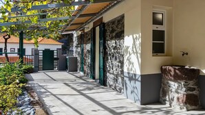 Ein überdachter Außenbereich mit Steinmauern, grünen Fensterläden und einem Betonweg.
