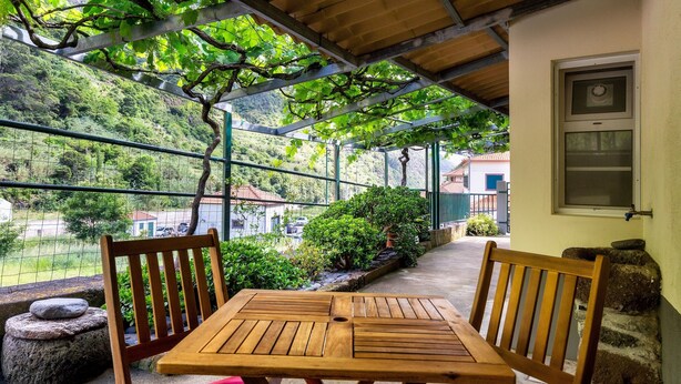 Ein Holztisch mit Stühlen unter einer Pergola mit Blick auf einen Hügel.