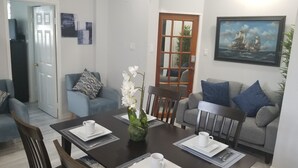 Spiseområde med et bord dækket til to personer, to sofaer, en dør og et maleri på væggen.