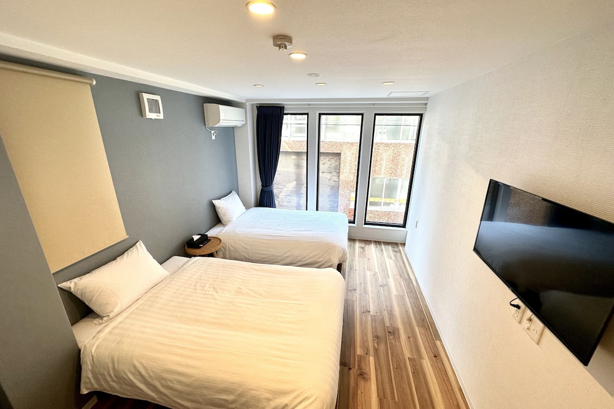 A hotel room with two beds, a TV, and a window with a view of the outside.