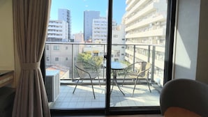 A balcony with two chairs and a small table, overlooking a cityscape with multiple buildings. - Ikoi Hotel Tokyo (Tokyo)