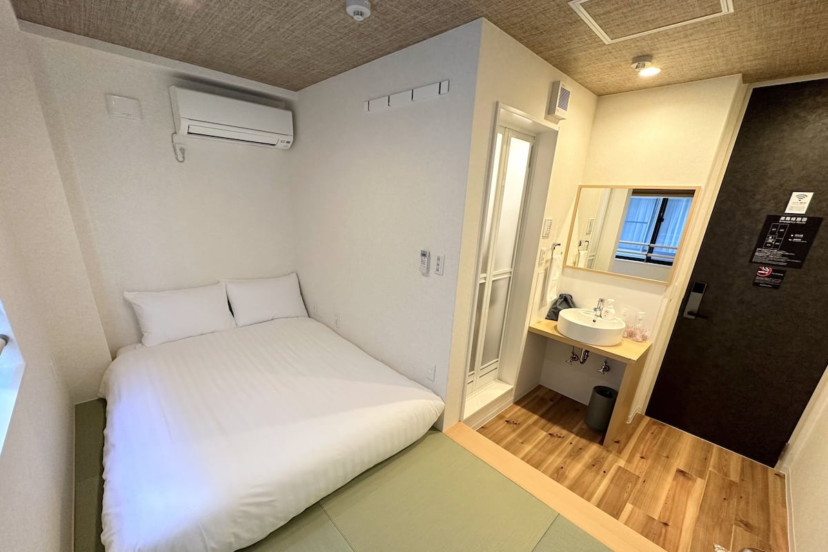 A bedroom with a bed, a bathroom with a sink and mirror, and a door leading to another room.