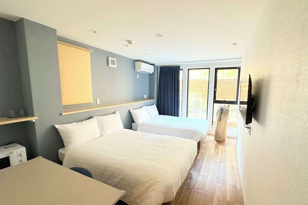 A hotel room with two beds, a desk, a microwave, and a TV.