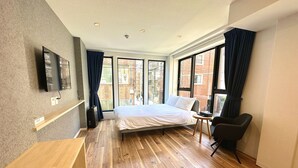 A modern hotel room with a wooden floor, a bed with white bedding, a desk, a chair, and large windows with curtains. - Ikoi Hotel Tokyo (Tokyo)