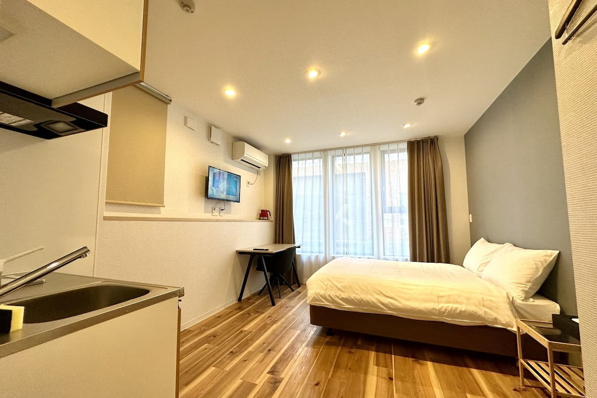 A compact hotel room with a bed, a desk, a TV, and a kitchenette.