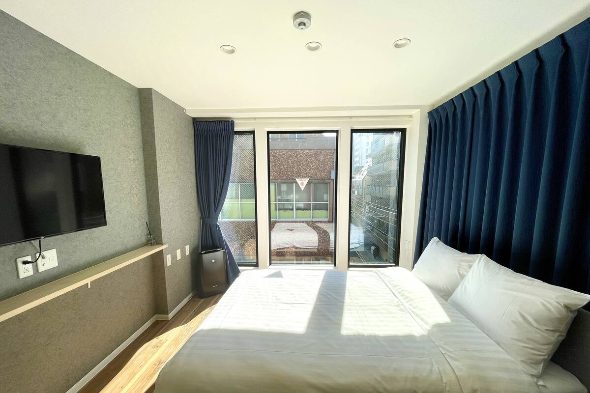 A hotel room with a large bed, a flat-screen TV mounted on the wall, and a sliding glass door leading to an outdoor area.