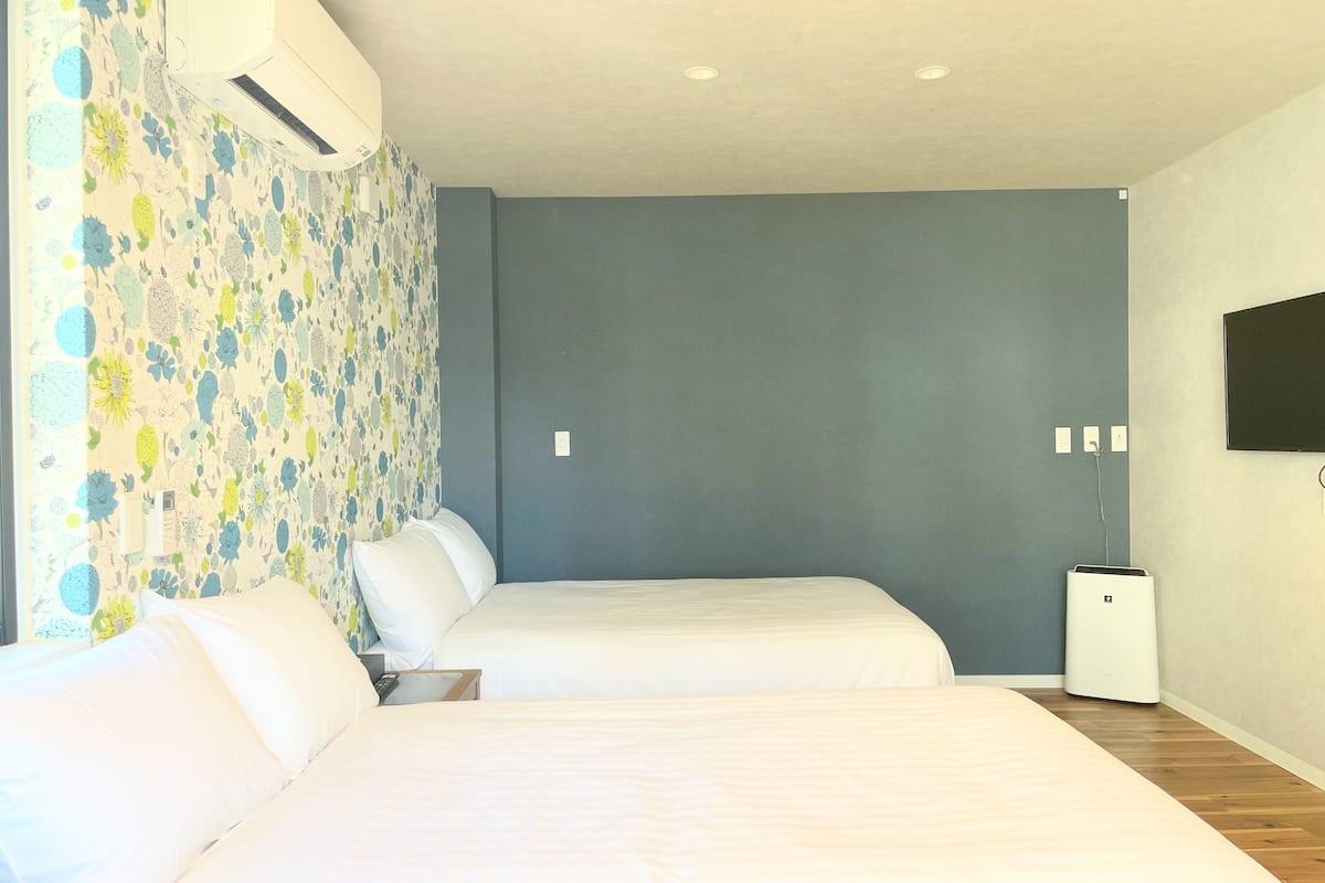 A hotel room with two beds, a TV on the wall, and a ceiling air conditioner.