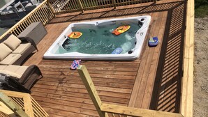 Une terrasse en bois avec un jacuzzi, des chaises longues et une planche de paddle.