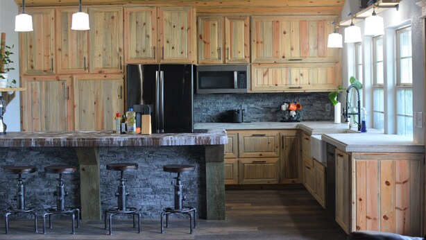 Une cuisine avec des meubles en bois, un îlot central doté de tabourets, un réfrigérateur, un four à micro-ondes et un évier.