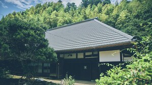 Een traditioneel Japans gebouw met een pannendak, omgeven door weelderige begroeiing en bomen.