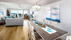 A spacious living area with a dining table, chairs, and a view of the ocean through large windows.