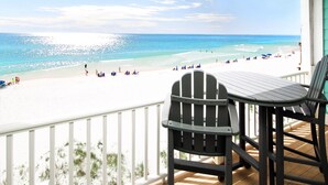 A balcony with a view of a beach, a table, and two chairs.