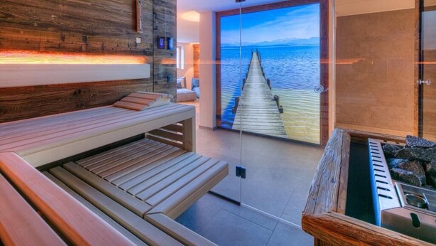 A modern spa room with a wooden bench, a view of a wooden pier extending into the sea, and a large window. - Gipfelhütte - mit Masterschlafzimmer, Zwei Hüttenzimmer und Balkon (Reit im Winkl)