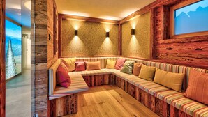 A cozy, wooden interior with a long bench and cushions, a large window with a mountain view, and wall-mounted lights. - Gipfelhütte - mit Masterschlafzimmer, Zwei Hüttenzimmer und Balkon (Reit im Winkl)