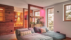 A modern living room with a sectional sofa, wooden walls, and large windows. - Gipfelhütte - mit Masterschlafzimmer, Zwei Hüttenzimmer und Balkon (Reit im Winkl)