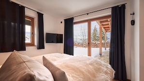 Un dormitorio moderno con una cama grande, un televisor de pantalla plana y vistas a un paisaje nevado a través de amplios ventanales.