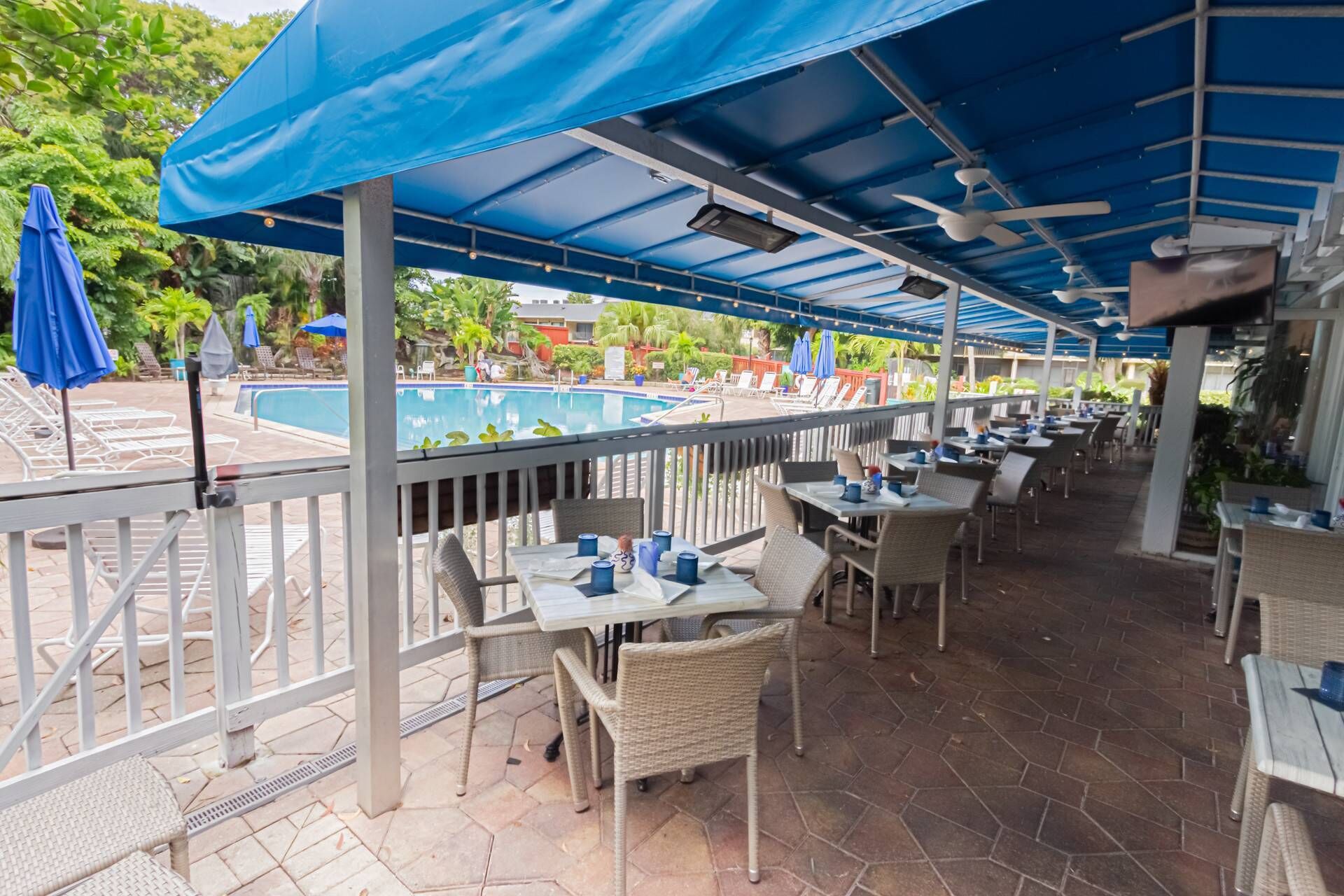Eine Außenpatio mit Tischen, Stühlen, einem Pool und Sonnenschirmen.