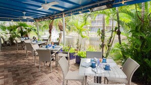 An outdoor patio with tables and chairs, surrounded by lush greenery and a water feature.