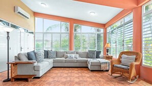Uma sala de estar com um sofá modular cinza, uma cadeira de balanço de vime e uma pequena mesa de madeira.