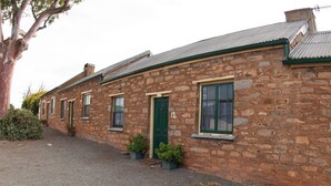 A row of stone buildings with a green door and windows, a gravel driveway, and a tree to the left. - Emma Tiver Heritage Cottage -restored Miner's Cottage - step back to circa 1856 (Burra)
