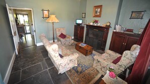 A living room with a fireplace, floral-patterned furniture, a television, and a bookshelf. - Emma Tiver Heritage Cottage -restored Miner's Cottage - step back to circa 1856 (Burra)