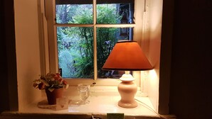 A window with a view of greenery, a potted plant, a glass, and a table lamp. - Emma Tiver Heritage Cottage -restored Miner's Cottage - step back to circa 1856 (Burra)