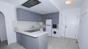 Une cuisine compacte avec des meubles gris, un évier encastré, un four à micro-ondes et un lave-linge.