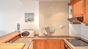 A kitchen with wooden cabinets, a microwave, a toaster, a hanging rack, and a stove. - A75 CALPPLACE ESC 1 5º 3 (Calpe)