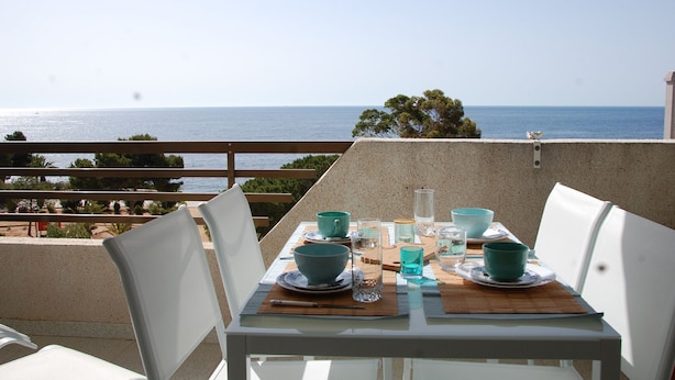A table set for two with teal bowls and glasses, overlooking a beach and the sea. - A75 CALPPLACE ESC 1 5º 3 (Calpe)