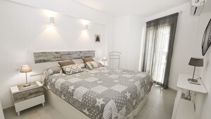Un dormitorio con cama, mesitas de noche, mesa auxiliar, aire acondicionado en la pared y una ventana con cortinas.