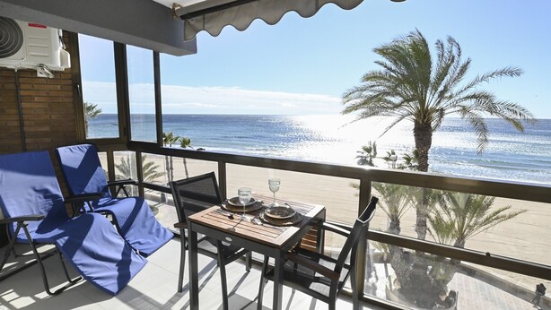 Un balcón con una mesa para dos, con vista a una playa con palmeras y el océano.