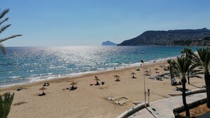Une plage avec des parasols et des chaises longues, un ciel dégagé et une montagne en arrière-plan.