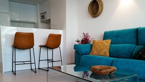 Un salon moderne avec un canapé turquoise, deux fauteuils marron, une table basse en verre et un tapis à motifs.