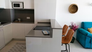 Une cuisine compacte équipée d’un micro-ondes, un petit coin repas avec deux chaises et un canapé bleu dans l’espace salon.