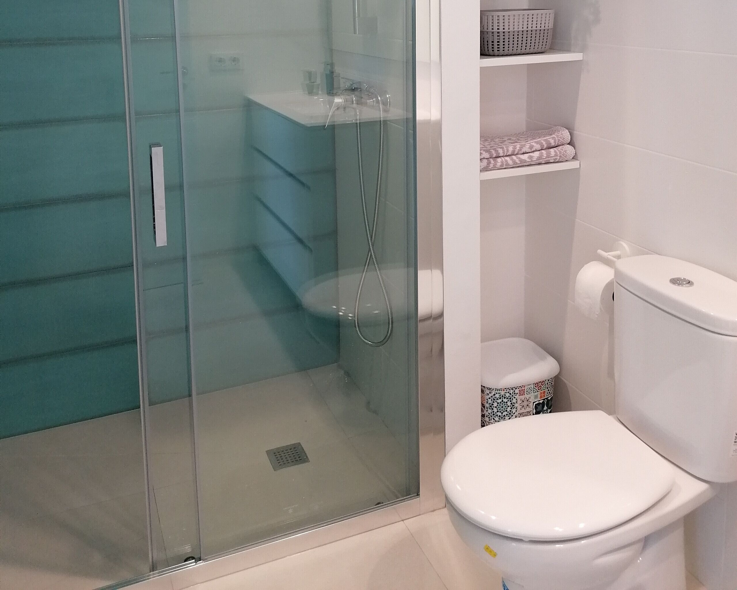 A bathroom with a glass-enclosed shower, a toilet, and a shelf with folded towels.