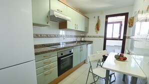 Una cucina con mobili verde chiaro, un piano di lavoro in granito, un fornello e un'area pranzo con tavolo e sedie bianche.