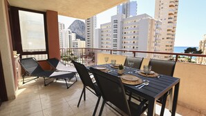 Un balcone con un tavolo apparecchiato per due, sedie e vista sulla città e sull'oceano.