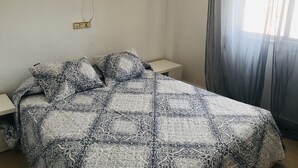 Un lit bien fait, avec une literie à motifs, une table de chevet et deux lampes fixées au mur.
