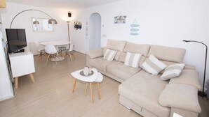 Un salon moderne comprenant un canapé, une table à manger avec des chaises, un téléviseur et une lampe.