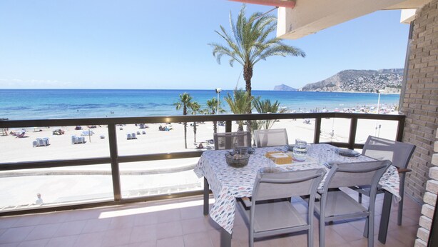 A balcony with a table and chairs, overlooking a beach with palm trees and a clear blue sky. - A38 CALPEMAR B 2º - 5 (Calpe / Calp)