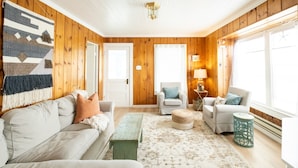 A cozy living room with a wooden paneled wall, a large rug, a sofa, two armchairs, a coffee table, and a lamp. - 2 Bedroom Vintage Beach Bungalow steps to downtown Rockaway and Rockaway Beach (Rockaway Beach)
