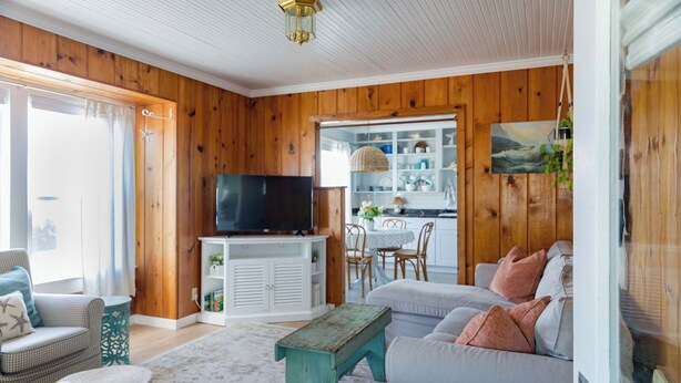 A cozy living room with a television, wooden walls, a dining area, and a view through a glass door. - 2 Bedroom Vintage Beach Bungalow steps to downtown Rockaway and Rockaway Beach (Rockaway Beach)