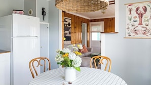 A dining area with a round table, white chairs, a wicker hanging light fixture, and a white refrigerator in the background. - 2 Bedroom Vintage Beach Bungalow steps to downtown Rockaway and Rockaway Beach (Rockaway Beach)