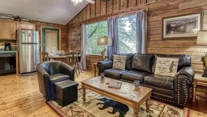 Un interno rustico di una baita, con arredamento in legno, un'area pranzo, un divano con cuscini decorativi e un tavolino da caffè.