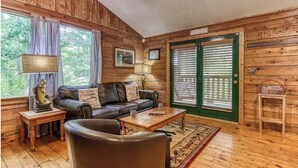 Un accogliente interno di una baita con un divano in pelle, pavimento in legno, un tavolino da caffè e una vista attraverso una porta verde.